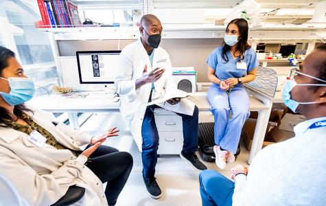 Shawn Hervey-Jumper, MD, in discussion with three members of his lab, who are seated around him.